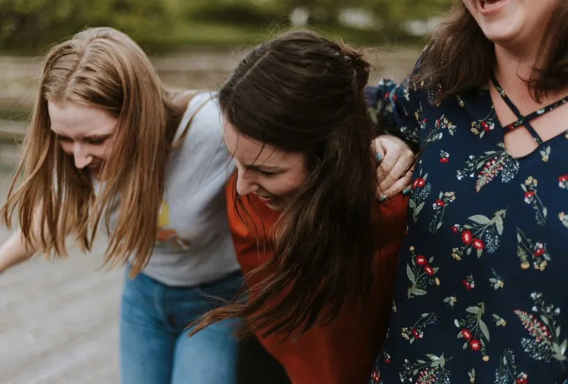 Trois adolescentes rient, bras dessus bras dessous, en extérieur